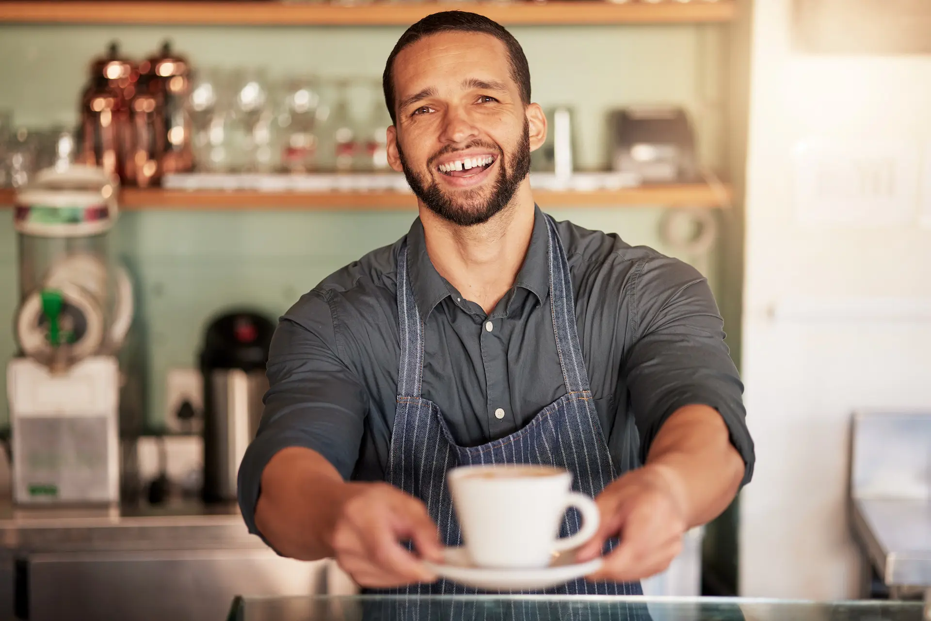 Barista zâmbitor care întinde o ceașcă de cafea peste tejghea