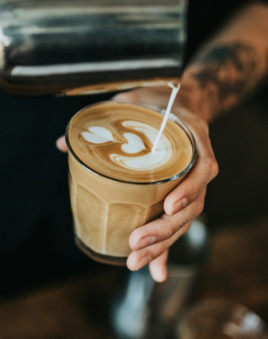 Barista care desenează latte art într-un pahar de cafea